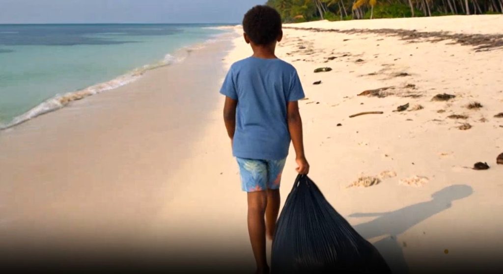 A young child pulling a black rubbish bag along a beach during a coastal clean-up