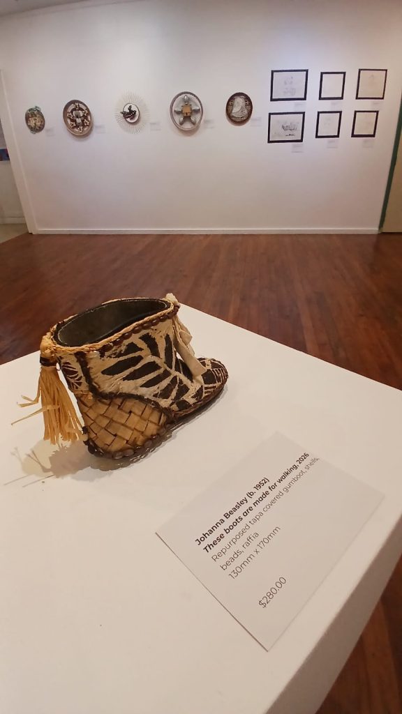 Johanna Beasley’s repurposed child’s gumboot artwork These Boots Are Made for Walking, 2026, displayed with drawings and assemblage works at the HOME+LAND exhibition