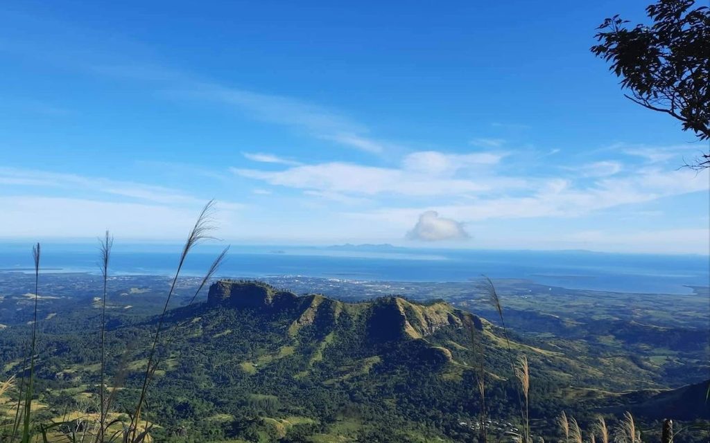 Table Top Mountain surrounded by forested ridges in Koroyanitu National Heritage Park near Lautoka, Fiji, with coastal plains, the Pacific Ocean and distant Mamanuca and Yasawa islands under a blue sky.